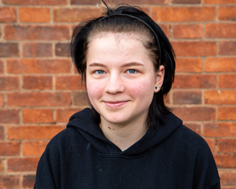 Young woman stands in front of brick wall