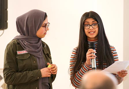 Young woman holds microphone as she speaks to a group