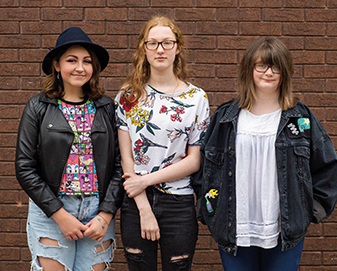Young women stand in front of a brick wall 