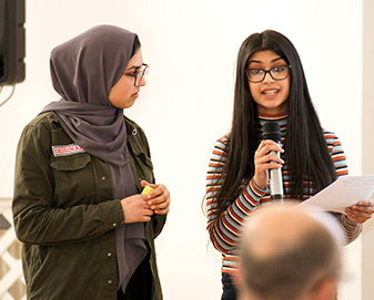 Young woman holds microphone as she speaks to a group