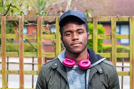 Young man with pink headphone stands in a garden